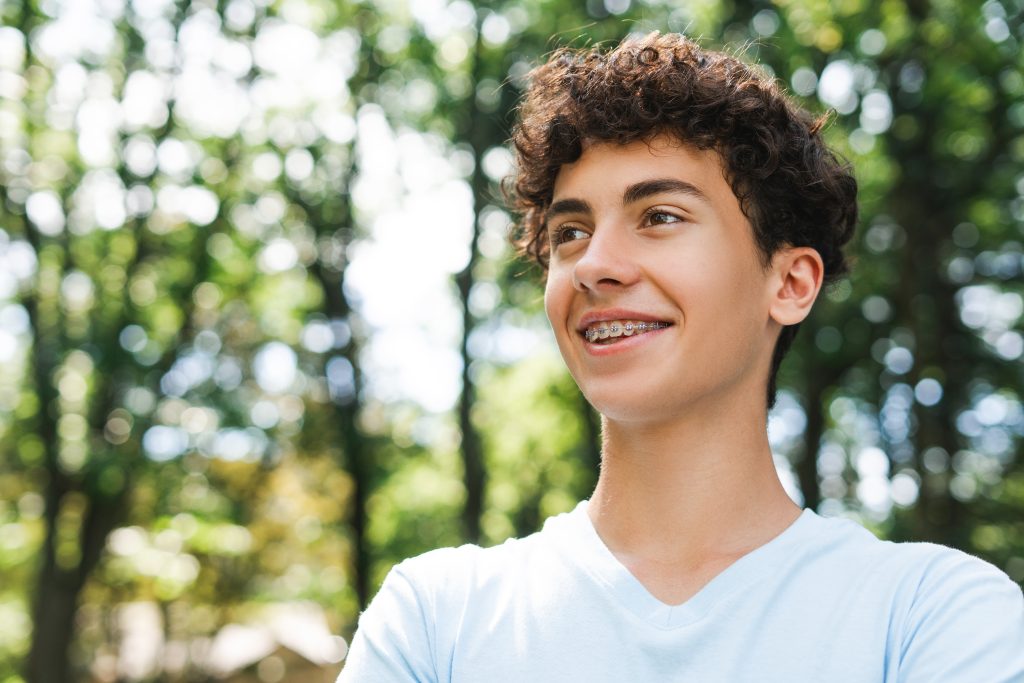 un adolescent souriant avec des appareils orthopediques regardant l espace de copie exterieur lateral